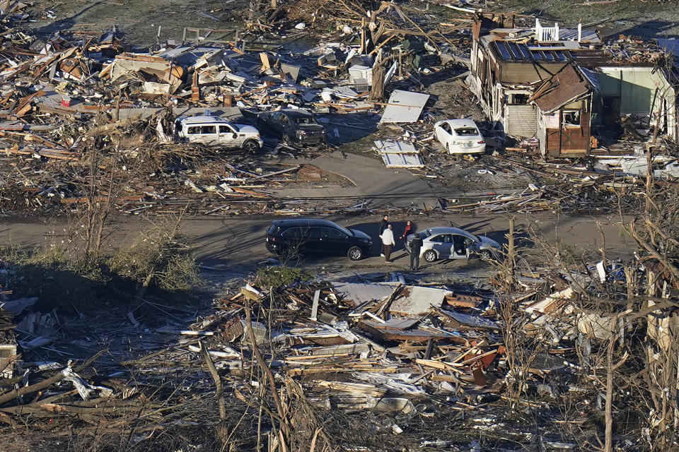 FILE - In a view from this aerial photo, people stand amidst destruction from a tornado in downtown Mayfield, Ky., on Dec. 12, 2021. Kentucky Gov. Andy Beshear says a rental housing shortage has gnawed at him since the recovery began from a tornado outbreak that hit western Kentucky in 2021. On Monday, June 3, 2024, Beshear unveiled plans to build 953 rental housing units in four counties — Christian, Graves, Hopkins and Warren. (AP Photo/Gerald Herbert, File)