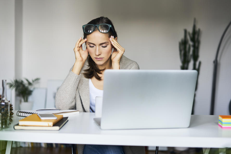 Young woman at home with laptop on desk touching her temples