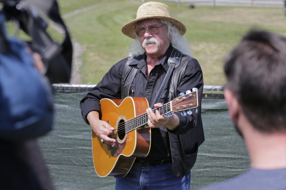 Woodstock veteran Arlo Guthrie plays a song at the original site of the 1969 Woodstock Music and Arts Fair in Bethel, N.Y., Thursday, Aug. 15, 2019. Guthrie is schedule to play a set on the top of hill nearby but told reporters he wanted to play at least one song on the original 1969 site. Woodstock fans are expected to get back to the garden to mark the 50th anniversary of the generation-defining festival. Bethel Woods Center for the Arts is hosting a series of events Thursday through Sunday at the bucolic 1969 concert site, 80 miles (130 kilometers) northwest of New York City. (AP Photo/Seth Wenig)