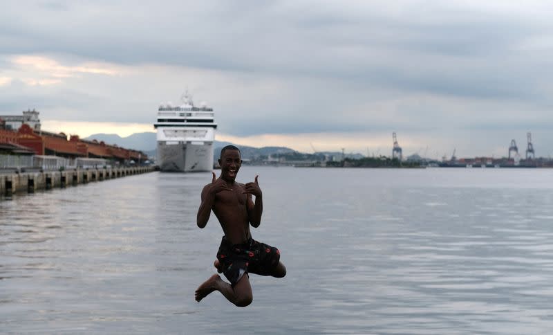 FILE PHOTO: A youth jumps into the waters of Guanabara Bay, next to a cruise ship docked at Rio de Janeiro port
