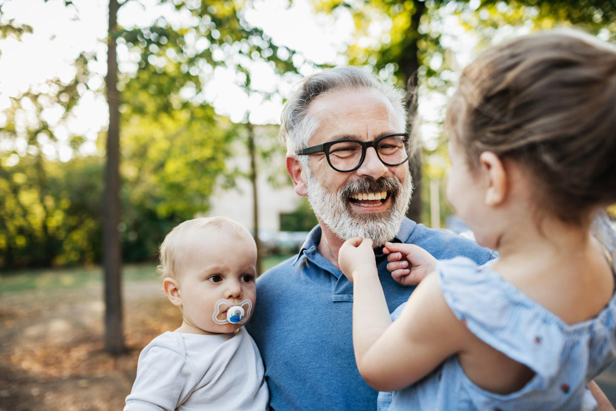 A grandfather holding and playing with two of his grandchildren while on a day out at the park together. boost longevity