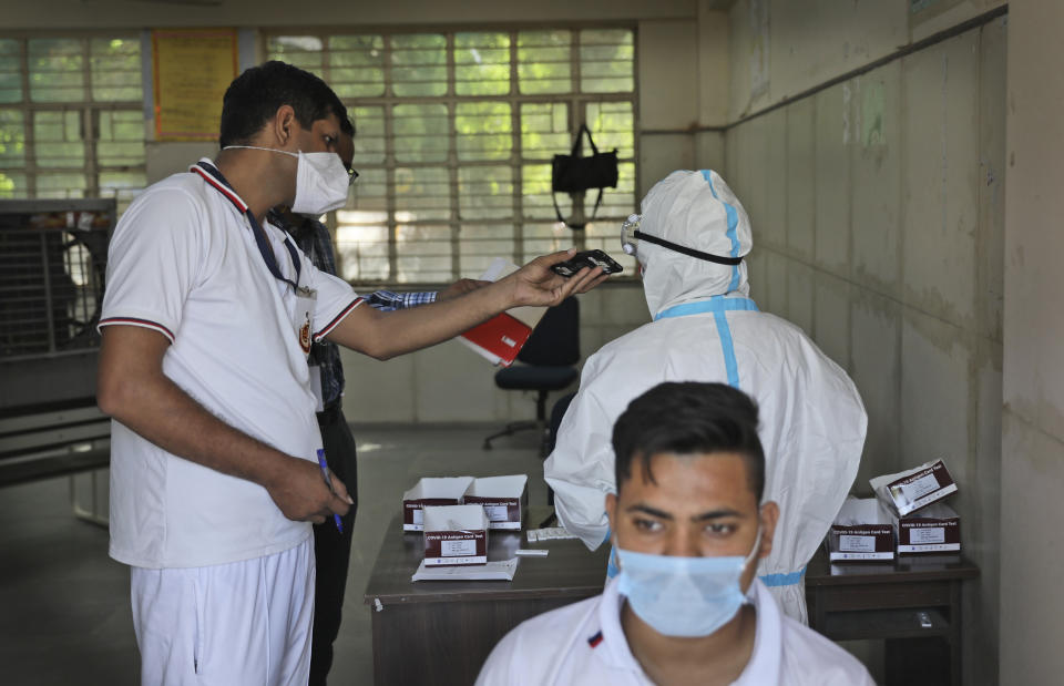 A Delhi police volunteer holds a mobile phone for a health worker as she takes an urgent call during testing for COVID-19 in New Delhi, India, Saturday, Oct. 3, 2020. India has crossed 100,000 confirmed COVID-19 deaths on Saturday, putting the country's toll at nearly 10% of the global fatalities and behind only the United States and Brazil. (AP Photo/Manish Swarup)