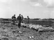 FILE - In this B/W file photo dated May 9, 1945, while American cities were going wild on an unconfirmed report of Germany's unconditional surrender, American soldiers and marines are checking the identification of their dead on May 9, 1945, on Okinawa, Japan. Resistance continues to be savage on this island in Japan's front yard. Following the defeat of the Nazis on May 8, 1945, Allied troops carried on fighting until Japan’s surrender, but many of them felt their efforts had not been fully recognized and dubbed themselves the “forgotten army.”(AP Photo/Sam Goldstein, FILE)