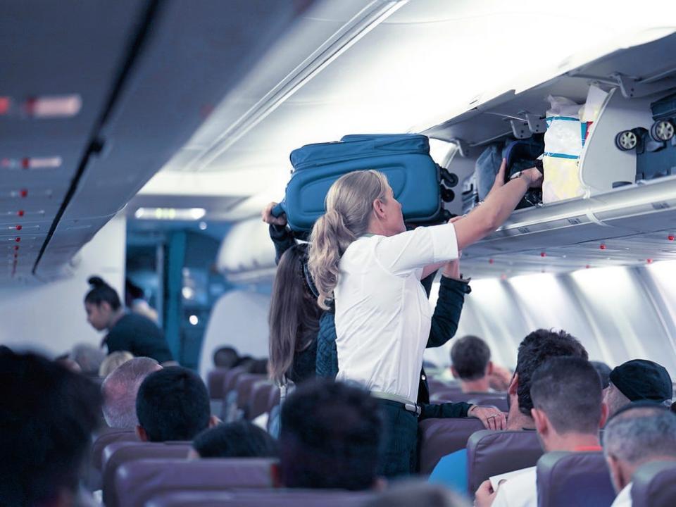 Flight attendant helps passengers stuff luggage into overhead bin