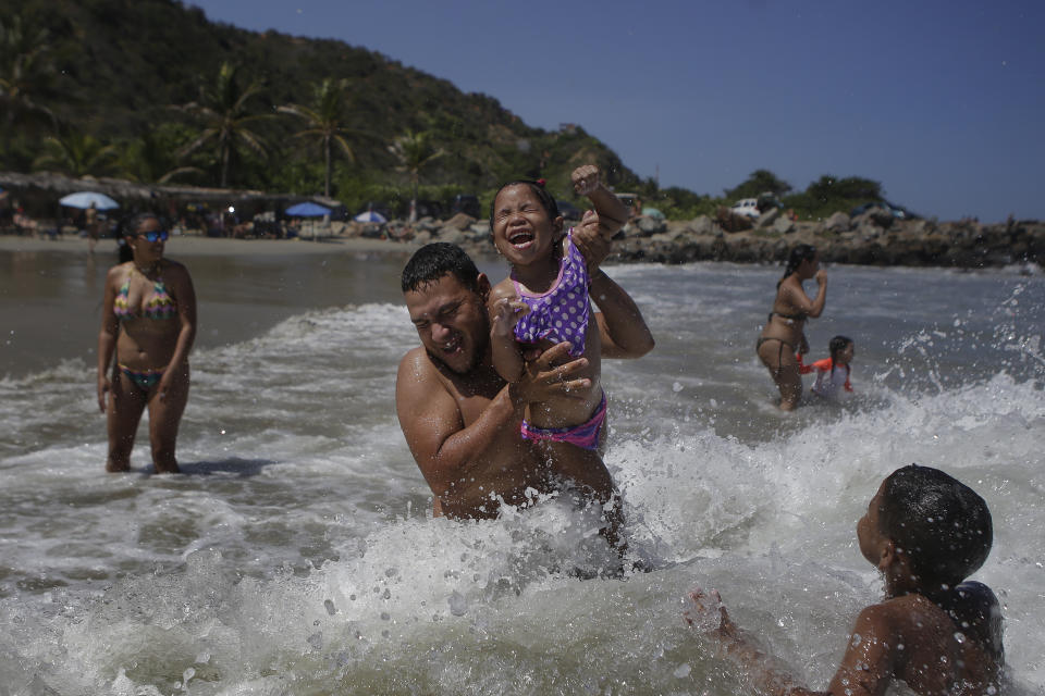 Caracas resident Jose Velasco lifts his daughter Ashley Velasco above a wave off La Ultima beach after it recently reopened following a lockdown to contain the spread of COVID-19 in La Guaira, Venezuela, Friday, Oct. 23, 2020. Strict quarantine restrictions forced the closure of beaches across the country in March and reopened this week. (AP Photo/Matias Delacroix)