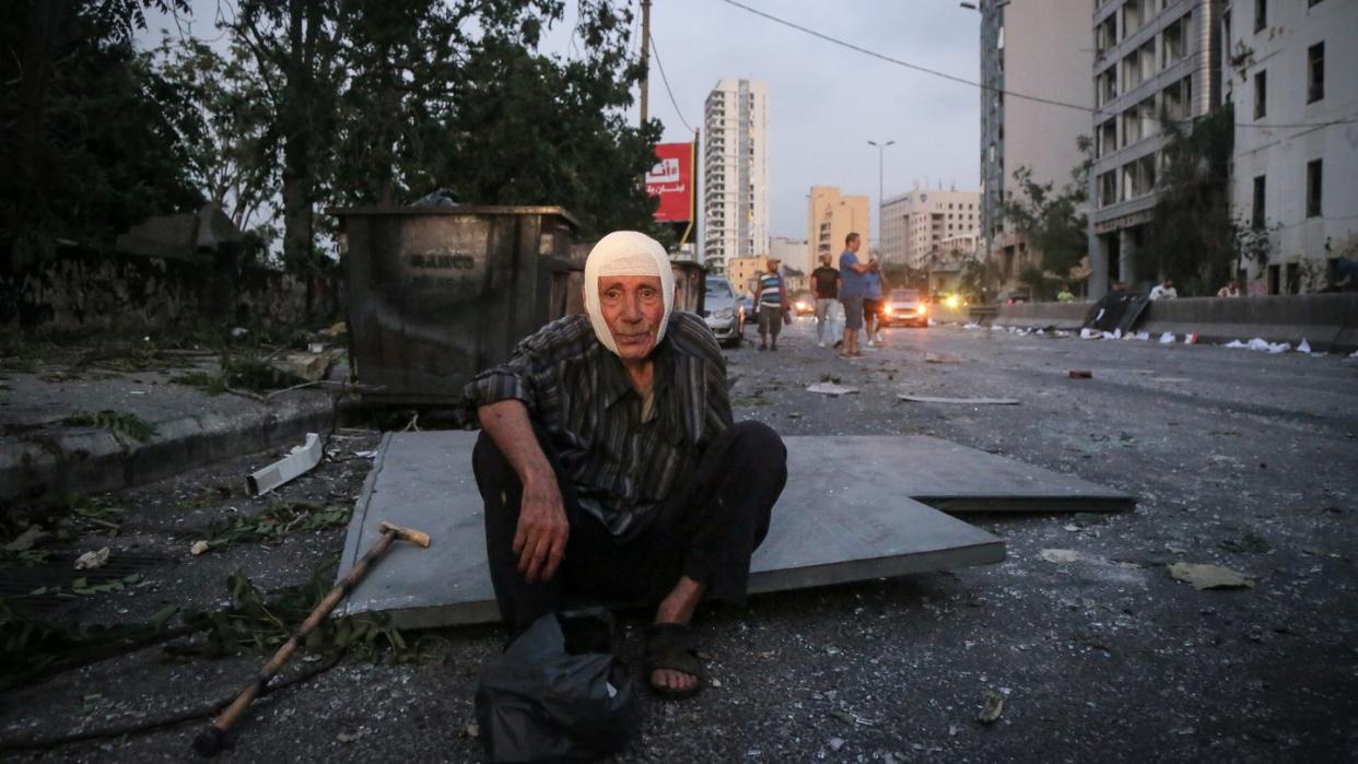 Ein älterer Herr sitzt nach der Explosion im Hafen von Beirut mit einem Verband auf dem Kopf auf der Straße.