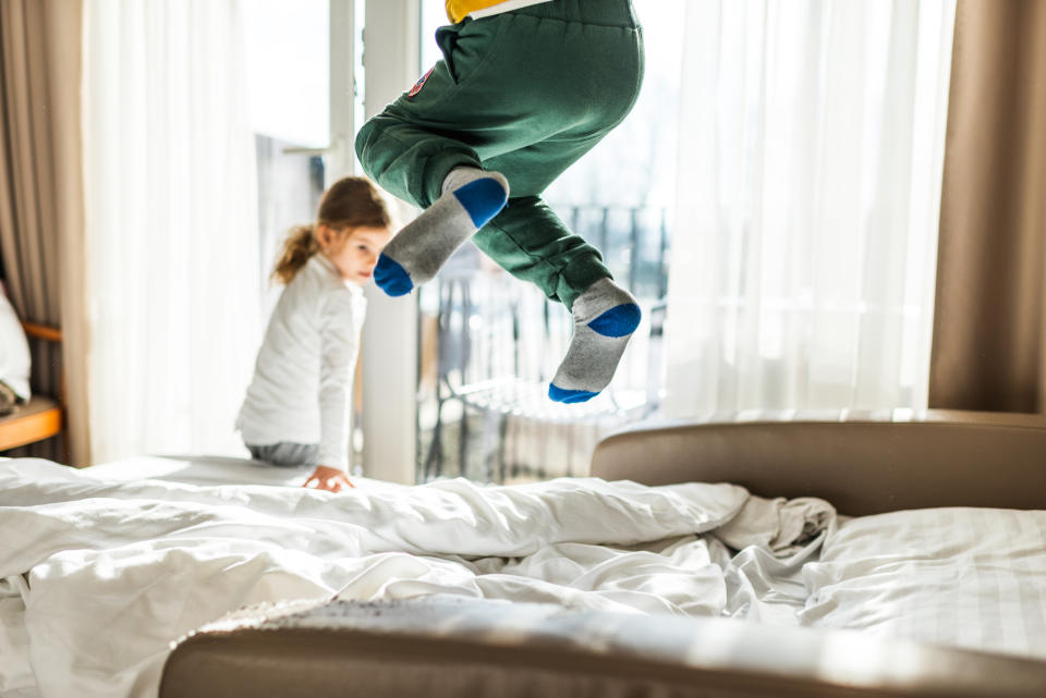 Child jumping on a bed, another child sitting and watching