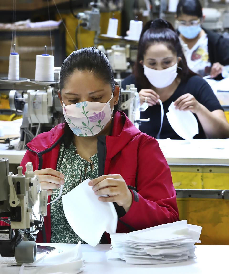 In this Thursday, April 23, 2020 photo, Romelia Barrientos, foreground, and other seamstresses work on edge binding and installing elastic on face masks at the Georgia Expo in Suwanee, Ga. The company has pivoted from sewing curtains to sewing cloth face masks. As business restrictions ease companies are preparing to open, but one key ingredient to safety is nearly impossible to find, personal protective equipment. (Curtis Compton/Atlanta Journal-Constitution via AP)