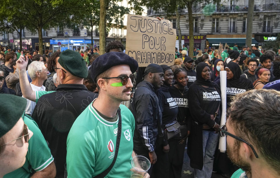 Protesters walk past an Irish rugby fan zone in Paris Saturday, Sept. 23, 2023. Activists from community groups, far-left parties and unions have held marches around France against racism and police brutality. Placard reads, "justice for Mahamadou." (AP Photo/Michel Euler)