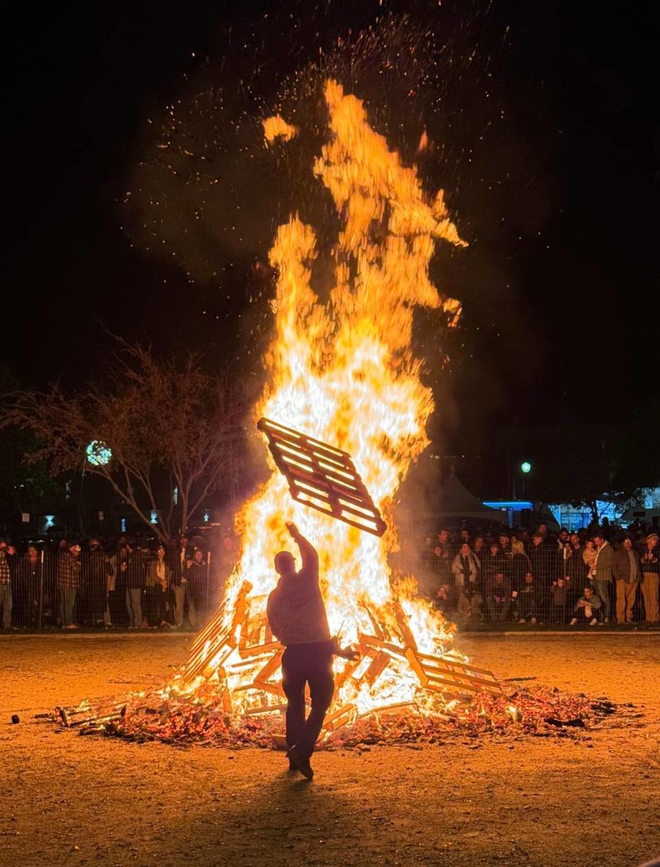 A firefighter throws a pallet onto the giant bonfire at Paso Robles’ New Year’s Eve celebration in the Downtown City Park on Dec. 31, 2023.