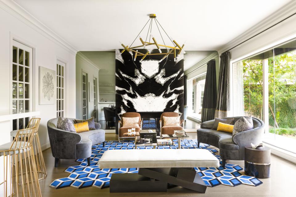 Curved sofas by Mitchell Gold + Bob Williams provide ample space for family gatherings. The irregular edges of the rug by Carol Piper play off the coffee tables by Tom Dixon and the brass chandelier by Jonathan Browning. The showstopper is undoubtedly the book-matched marble slabs that surround the fireplace. A closer look reveals that the black-and-white stone doesn’t quite reach the ceiling. “The marble slabs were eight inches too short, so I had the contractor fill the space with wood and I hired an artist to paint the space,” Loya explains of the faux design moment. “I had to improvise!”