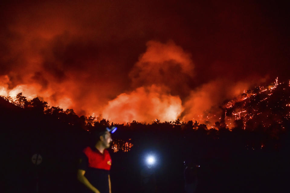 A man leaves as advancing fires rage the Hisaronu area, Turkey, Monday, Aug. 2, 2021. For the sixth straight day, Turkish firefighters battled Monday to control the blazes that are tearing through forests near Turkey's beach destinations. Fed by strong winds and scorching temperatures, the fires that began Wednesday have left eight people dead. Residents and tourists have fled vacation resorts in flotillas of small boats or convoys of cars and trucks. (AP Photo)