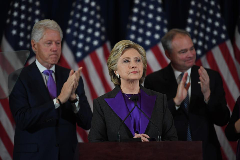 Hillary Clinton stands at a podium flanked by Bill Clinton and Tim Kaine.