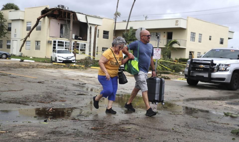 A man and a woman walk through the parking lot of a condominium complex damaged by an apparent tornado