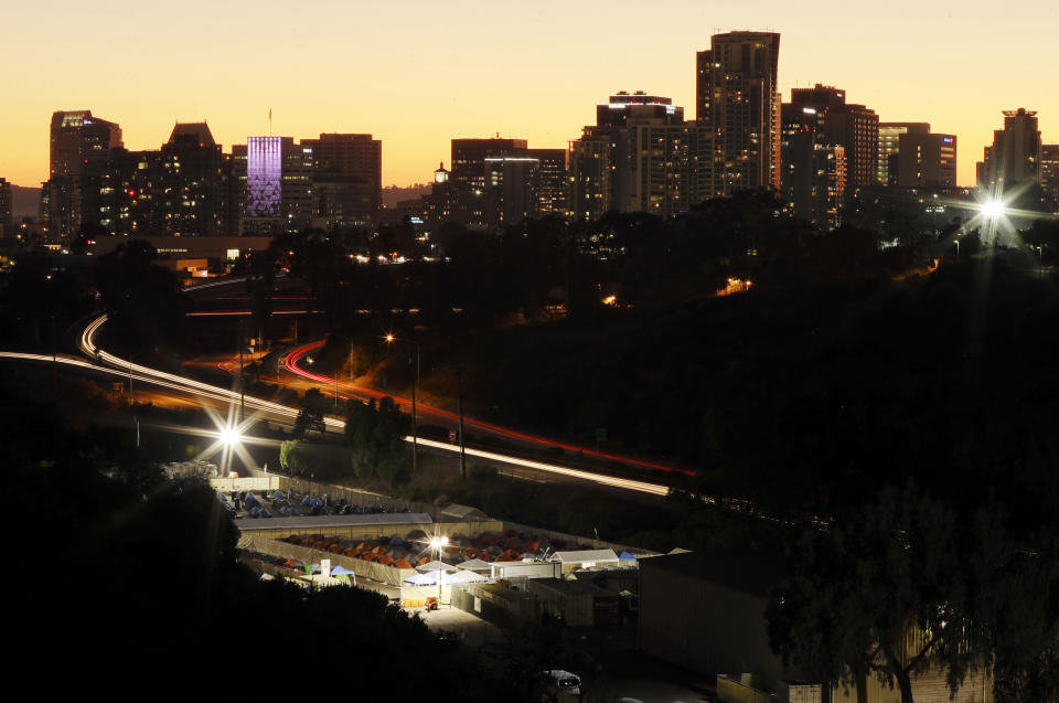 FILE - In this Oct. 26, 2017, file photo, the city-sanctioned tent encampment, below, used to get people off the streets, sits on the edge of Balboa Park as the sun sets behind buildings downtown in San Diego. A new federal report says the number of people living on the streets in Los Angeles and San Diego, two epicenters of a West Coast homelessness crisis, fell this year, suggesting possible success in those cities' efforts to combat the problem. Homelessness overall was up slightly across the country, although the report did not provide a complete picture of the problem. (AP Photo/Gregory Bull, File)