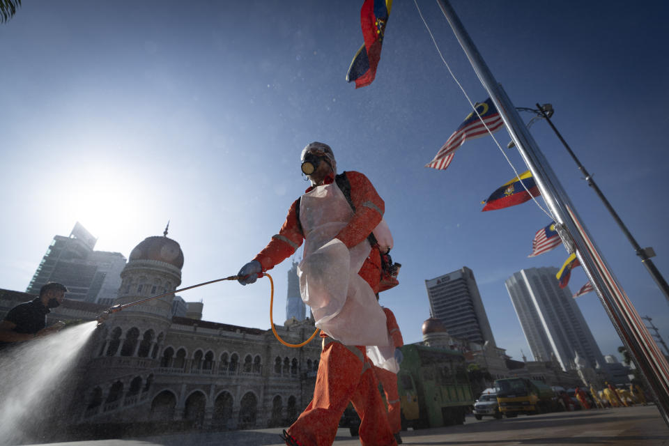 A city hall worker sprays a disinfectant at Merdeka Square, or independence square, situated in front of the Sultan Abdul Samad Building, background, in Kuala Lumpur, Malaysia, Saturday, Oct. 17, 2020. Malaysia will restrict movements in its biggest city Kuala Lumpur, neighboring Selangor state and the administrative capital of Putrajaya from Wednesday in an attempt to curb a sharp rise in coronavirus cases. (AP Photo/Vincent Thian)