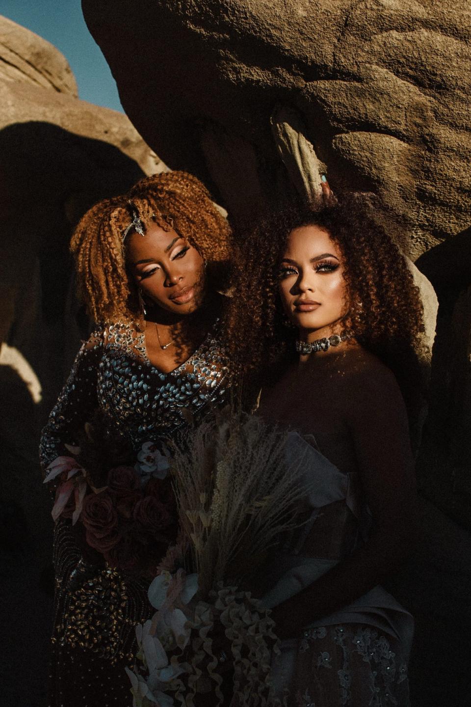 Two brides pose in front of desert rocks on their wedding day.