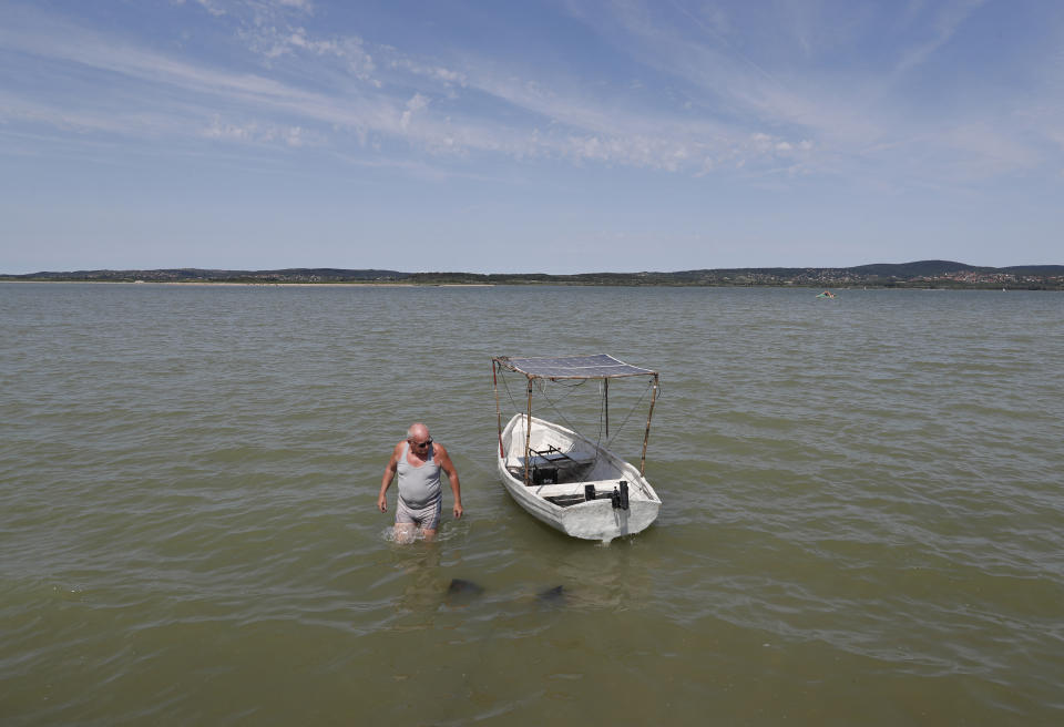 A man walks out from his homemade boat in the Lake Velence in Agard, Hungary, Sunday, Aug. 8, 2021. Activists and environmental experts in Hungary say the effects of climate change and insufficient infrastructure are colliding to threaten the country’s third largest natural lake with an economic and ecological crisis. Lake Velence has lost nearly half of its water in the last two years as hot, dry summers have led to increased evaporation and deteriorating water quality. (AP Photo/Laszlo Balogh)