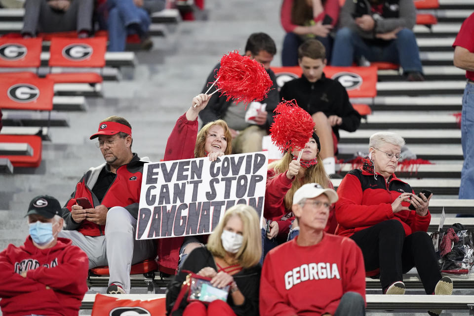 FILE - In this Oct. 3, 2020, file photo, a fan holds a sign "Even COVID can't stop Dawgmation" before an NCAA college football game, in Athens, Ga. Coaches wearing masks around their chins. Fans not wearing masks at all while cheering from their seats. One school deciding to drop the safety checks it was requiring for those entering the stadium to cut down on long lines. College football is sending plenty of alarming signals at it attempts to get through a tenuous season amid a pandemic. (AP Photo/Brynn Anderson, File)