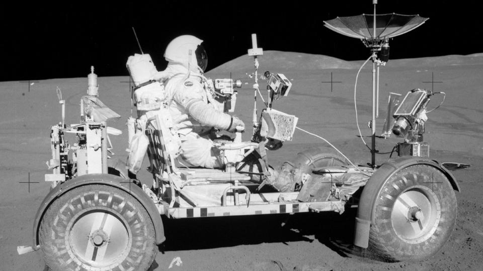 an astronaut in a space suit driving a car-like vehicle without a roof