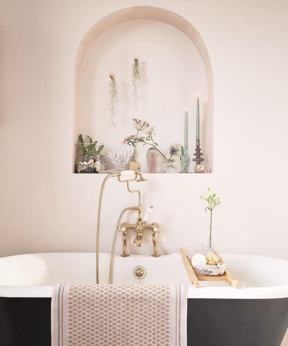 bathroom with traditional roll top bath and an arched niche housing plants, flowers and candles