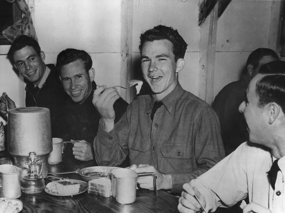 A black and white photo of a young man with a fork in hand surrounded by other young men.