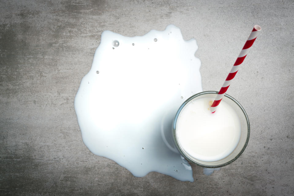 Glass of milk and a red and white drinking straw on a concrete table. It is a puddle of milk on the table. Crying over spilt milk. View from the above.