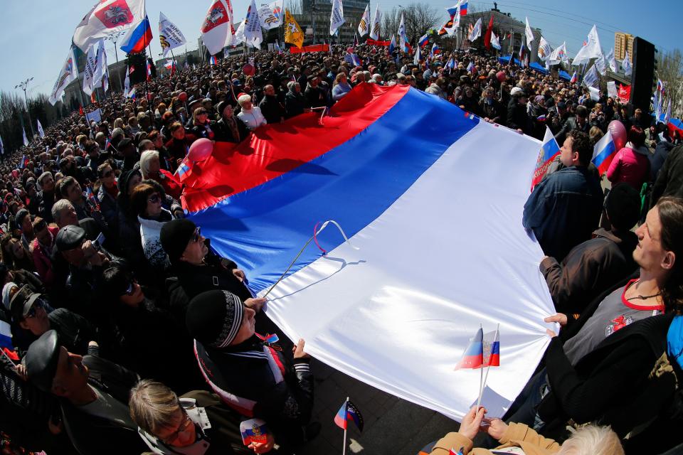 Pro-Russian activists hold a huge Russian national flag in front of the regional administration building in Donetsk, Ukraine, Sunday, April 6, 2014. In Donetsk a large group of people surged into the provincial government building and smashed windows. A gathering of several hundred, many of them waving Russian flags, then listened to speeches delivered from a balcony emblazoned with a banner reading a "Donetsk Republic". (AP Photo/Andrey Basevich)