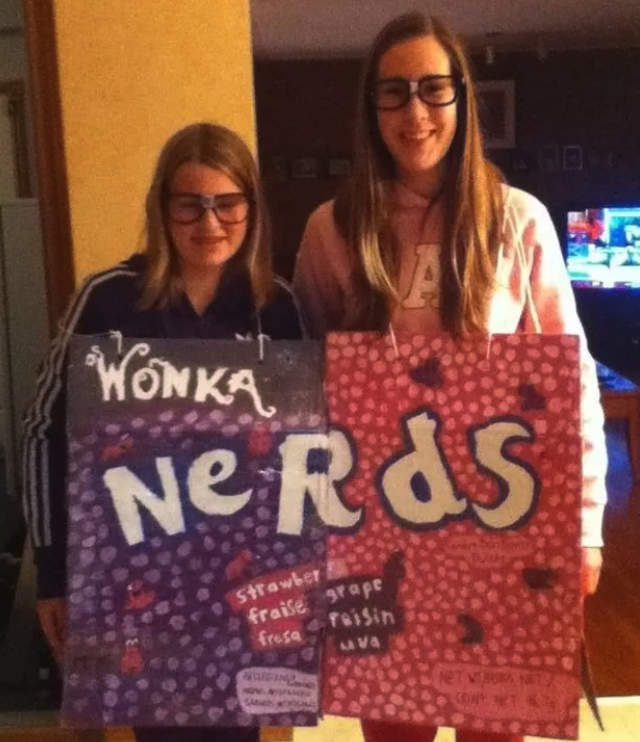 Two people with a poster board attached to them with a hand-drawn Nerds logo on it