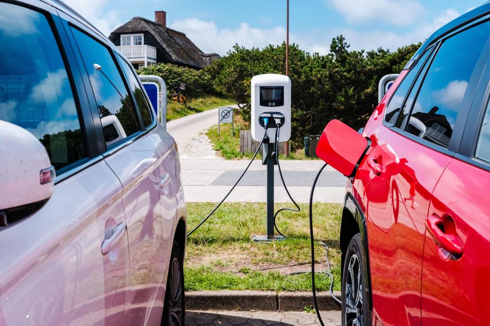 Billum, Denmark - August 8, 2023: Two cars connected by cable to an electric charging pole.