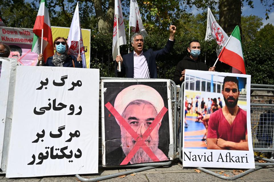 Protesters wave the Lion and Sun flag of the National Council of Resistance of Iran and the white flag of the People's Mujahedin of Iran, two Iranian opposition groups, with a placard depicting the crossed out face of Iran's President Hassan Rouhani as they demonstrate outside the Iranian embassy in London on September 12, 2020 against the execution of Iranian wrestler Navid Afkari in the southern Iranian city of Shiraz and against the Iranian government. - Iran said it executed wrestler Navid Afkari, 27, on September 12, 2020 at a prison in the southern city of Shiraz over the murder of a public sector worker during anti-government protests in August 2018. Reports published abroad say Afkari was condemned on the basis of confessions extracted under torture, prompting online campaigns of support for his release. (Photo by JUSTIN TALLIS / AFP) (Photo by JUSTIN TALLIS/AFP via Getty Images)