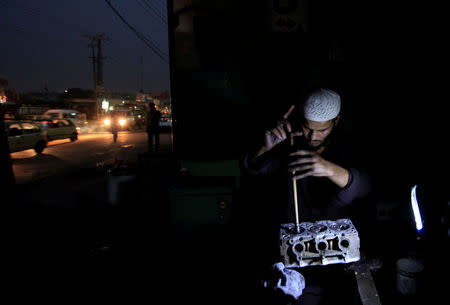 A mechanic uses a battery operated light to illuminate an engine as he performs repairs during a power outage in Rawalpindi, Pakistan, October 4, 2016. REUTERS/Faisal Mahmood