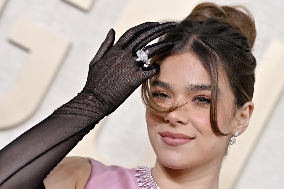 A close up image of a girl using her hand to move her hair from her face. She is wearing black sheer gloves with a ring over, and a pink dress