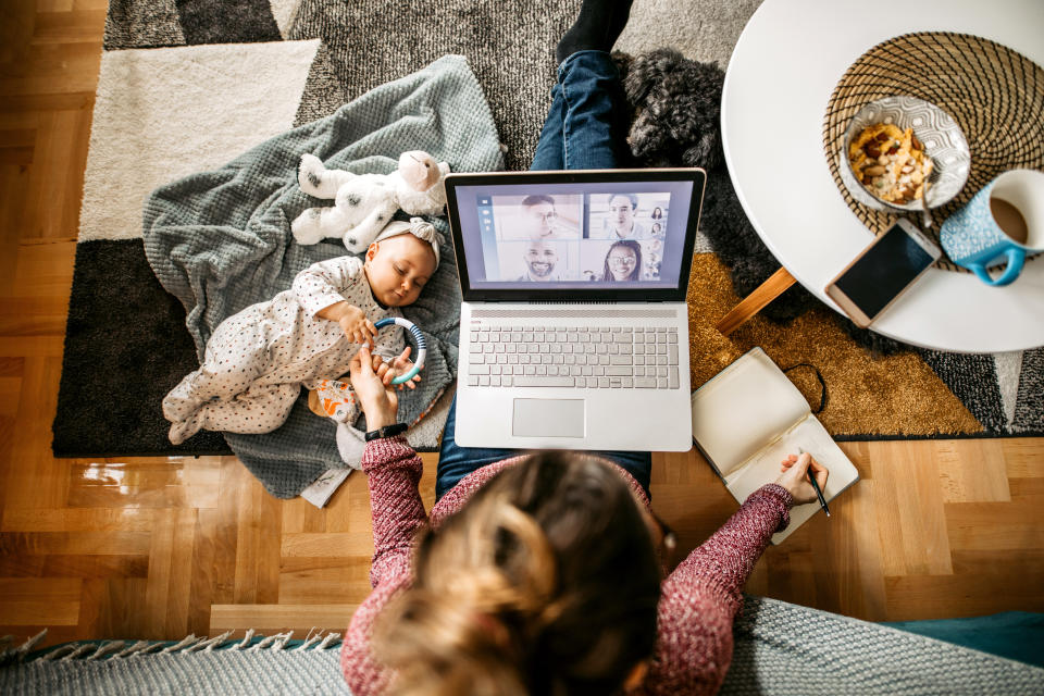 Cute little baby playing on the floor by her working mother.  Young mother with a baby and a dog, sitting on the floor and working. High angle of view.