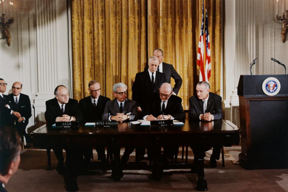 historical photo of president lyndon b johnson sitting at a long desk on a stage with other men in suits representing the united kingdom and u.s.s.r. signing a treaty