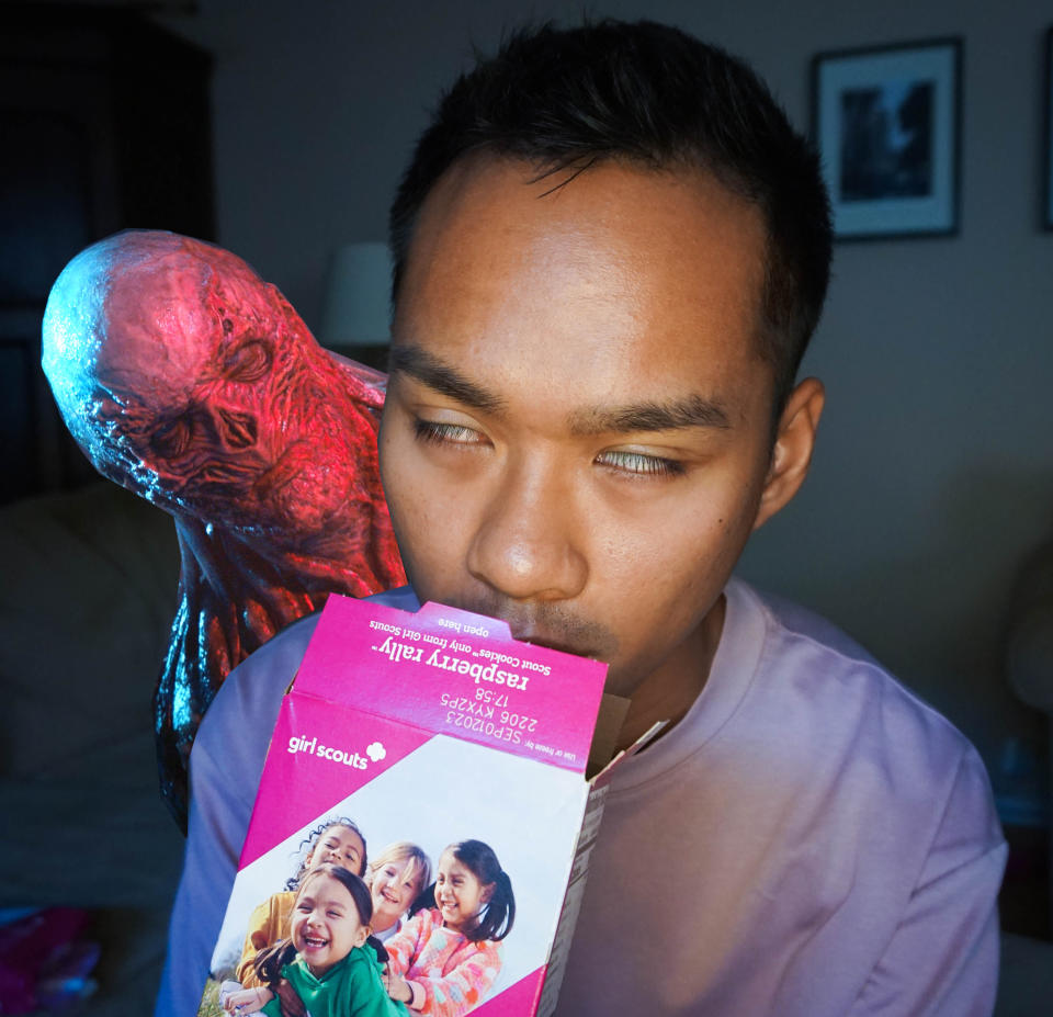 author sniffing an open box of raspberry rally girl scout cookies and rolling his eyes back with happiness with vecna from "stanger things 4" lurking behind him