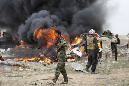 Shi'ite fighters known as Hashid Shaabi walk as smoke rises from an explosives-laden military vehicle driven by an Islamic State suicide bomber which exploded during an attack on the southern edge of Tikrit, Iraq in this March 12, 2015 file photo. REUTERS/Thaier Al-Sudani/Files