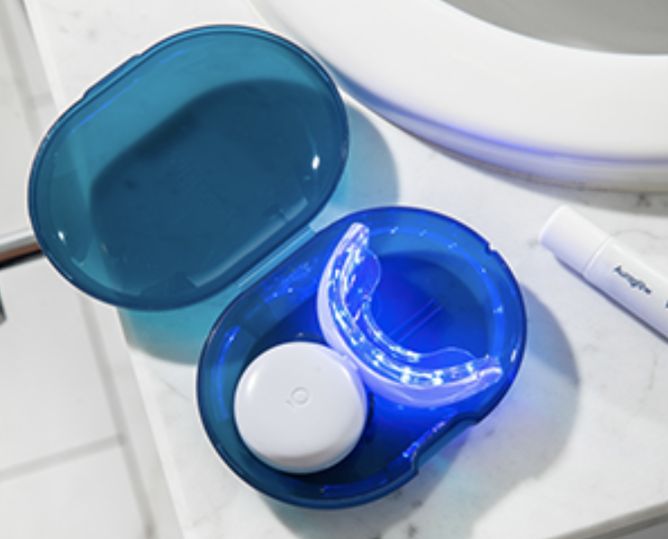 A teeth whitening mouth tray glows blue on a white bathroom countertop.