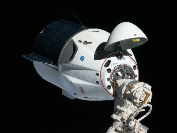 The white and black Dragon 2 space capsule in space, with the nose hatch open.