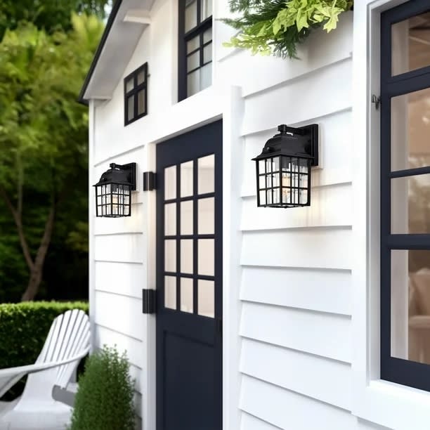 Black sconces on white siding flanking a black door