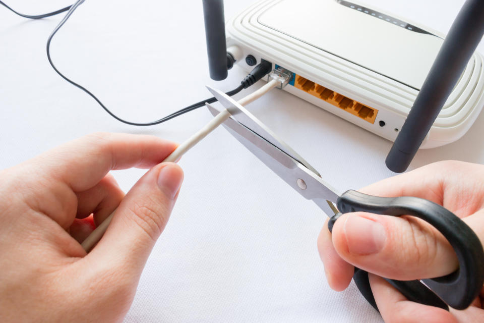 A person cutting Internet cable connected to a router.