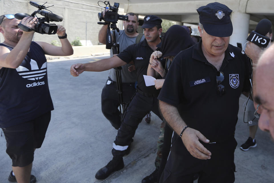 Elite police unit officers escort a 19-year old British woman, center with head covered, to Famagusta court in Paralimni, Cyprus, Tuesday, July 30, 2019. The British woman faces a public nuisance charge after she admitted that her accusation that 12 Israeli teens raped her at a popular resort town was untrue. (AP Photo/Petros Karadjias)