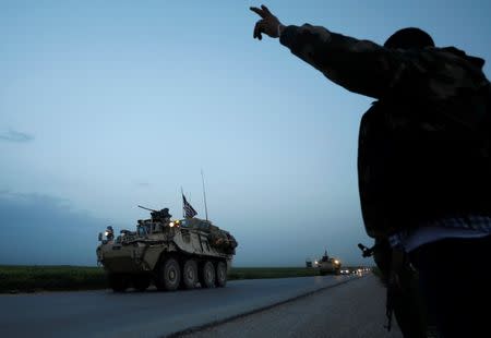 A Kurdish fighter from the People's Protection Units (YPG) gestures at a convoy of U.S military vehicles driving in the town of Darbasiya next to the Turkish border, Syria April 28, 2017. REUTERS/Rodi Said