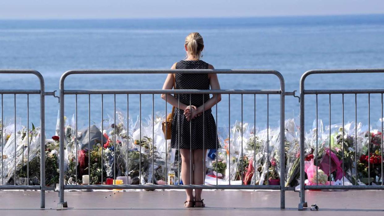 A woman stands by the new makeshift memorial in tribute to the victims of the deadly Bastille Day attack at the Promenade des Anglais on July 19, 2016 in Nice, after it was moved from the pavement of the road to the seafront so that the street can be re-opened. - The Islamic State group claimed responsibility for the truck attack that killed 84 people in Nice on France's national holiday, a news service affiliated with the jihadists said on July 16. Tunisian Mohamed Lahouaiej-Bouhlel, 31, smashed a 19-tonne truck into a packed crowd of people in the Riviera city celebrating Bastille Day -- France's national day. (Photo by Valery HACHE / AFP)