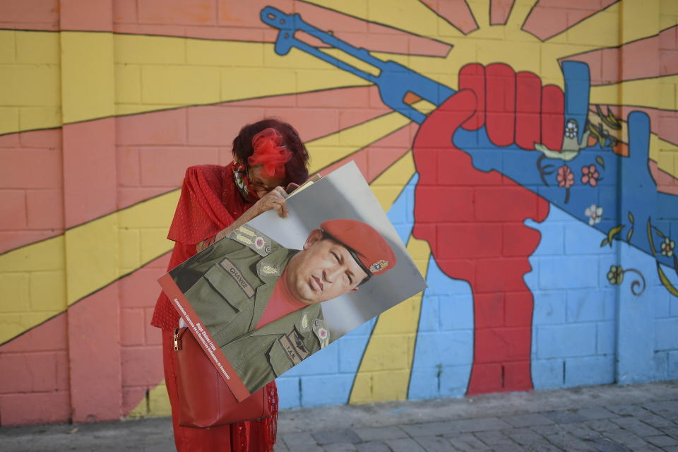 A government supporter known as "Caperucita," or Little Red Riding Hood, holds a photo of late Venezuelan President Hugo Chavez as she looks for something in her purse in Plaza Bolivar, near the National Assembly where newly elected National Assembly lawmakers will be sworn-in and hold their first session of the year in Caracas, Venezuela, Tuesday, Jan. 5, 2021. (AP Photo/Matias Delacroix)
