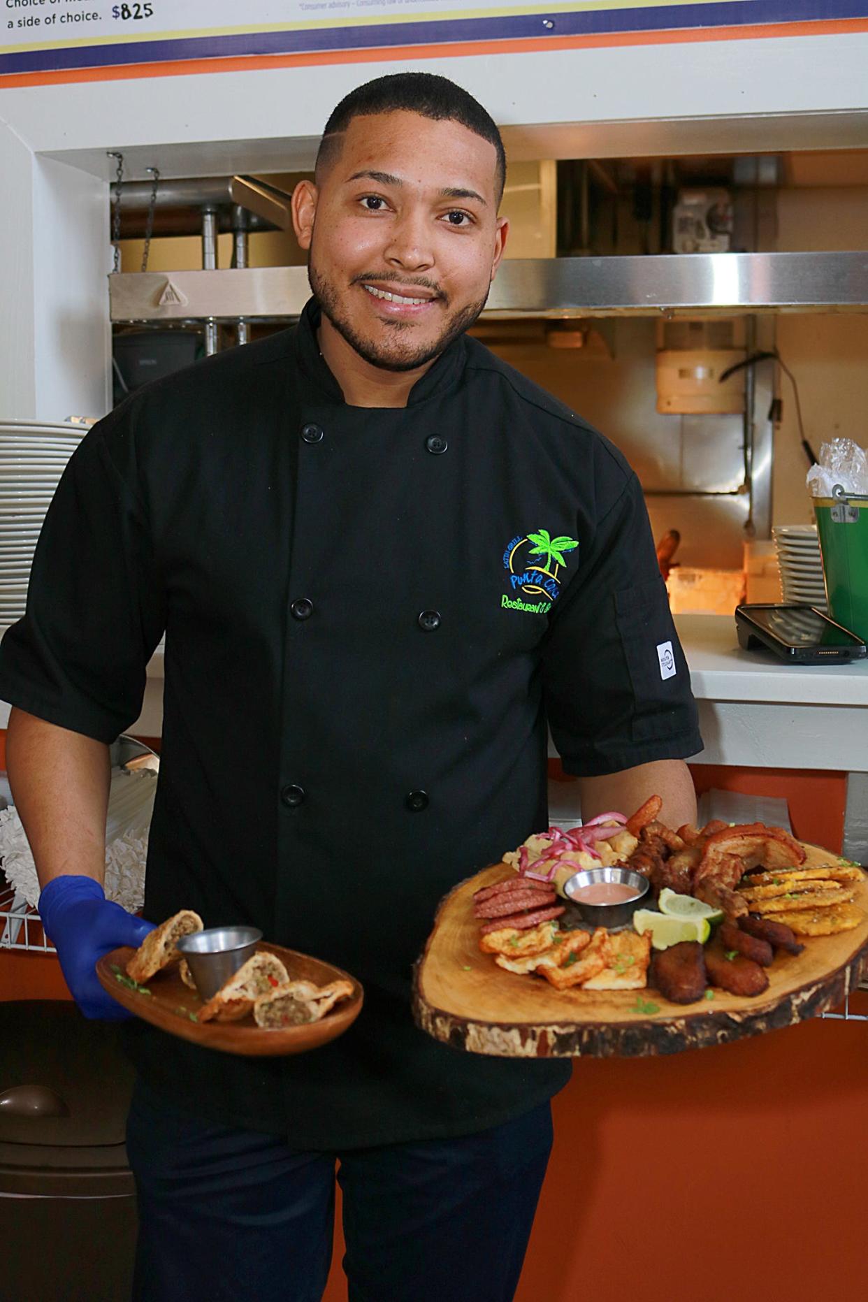 Punta Cana Latin Grill co-owner and chef Frank Cambero holds sample plates featuring empanadas, fried yucca, tostones, maduros, and a variety of Dominican seasoned meats.