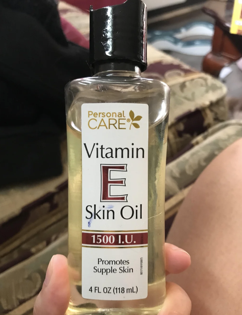 Person holding a bottle of vitamin E skin oil with a detailed label, resting on their lap.