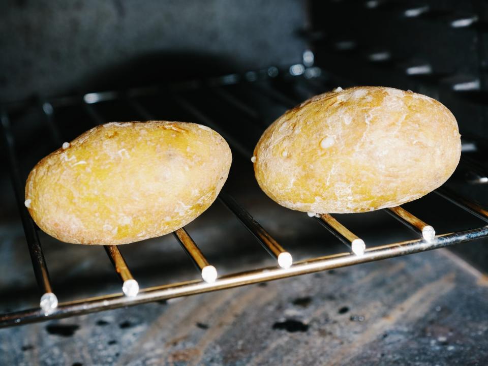 Two potatoes baking in an oven directly on the rack