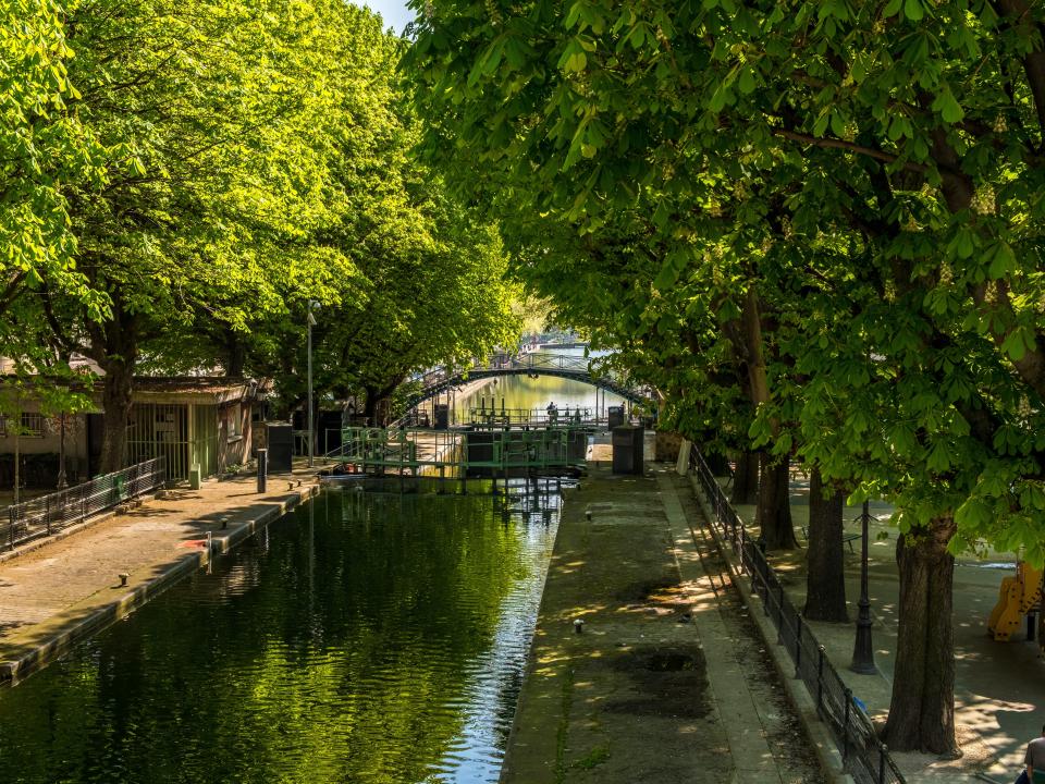 Trees and houses surround a canal with an arched bridge in distance