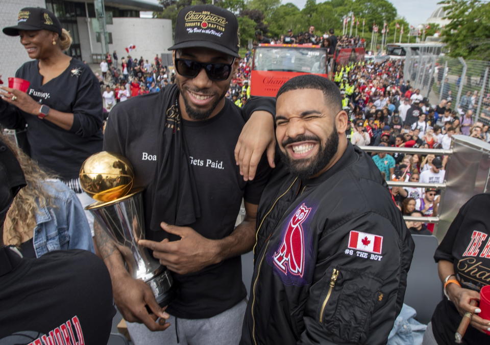 FILE - Toronto Raptors' Kawhi Leonard, front left, holds his MVP trophy while posing with rapper/producer Drake as they celebrate during the team's NBA basketball championship parade in Toronto, June 17, 2019. Just as a movie soundtrack helps viewers follow the action of the narrative through each plot twist, hip-hop has done the same for basketball via the NBA. Drake has been a global ambassador for his hometown team the Toronto Raptors since 2013 and is often seen on the sidelines interacting with coaches and players. (Frank Gunn/The Canadian Press via AP, file)